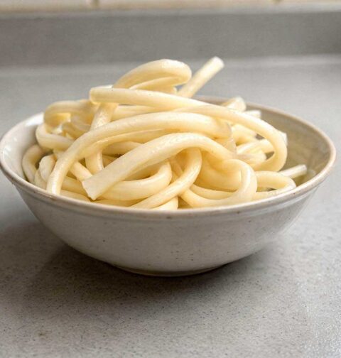 Een wit schaaltje met daarin gekookte udon noedels.