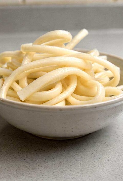 Een wit schaaltje met daarin gekookte udon noedels.