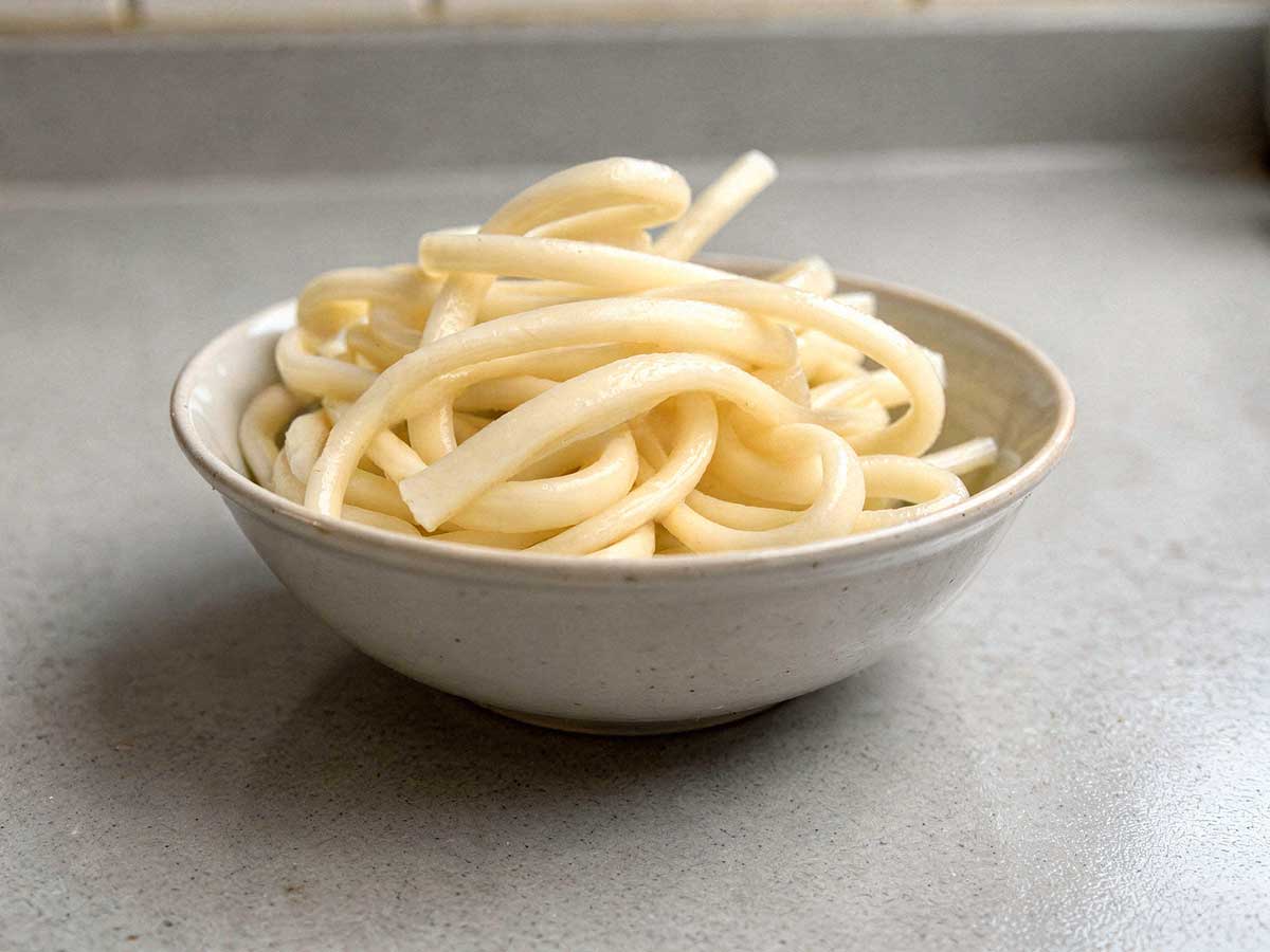 Een wit schaaltje met daarin gekookte udon noedels.