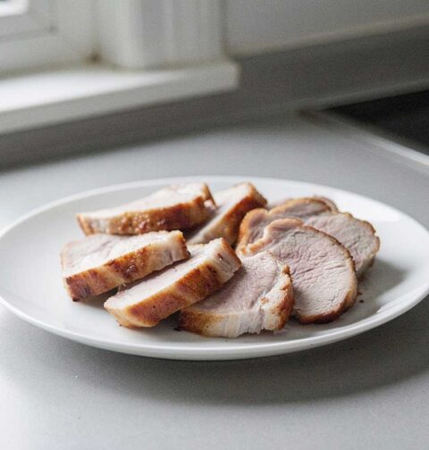 Plakken gebakken varkensfilet mooi neergelegd op een wit bordje.