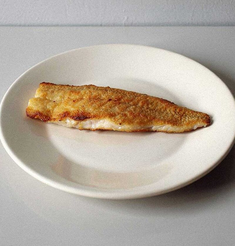 Een gebakken wijtingfilet op een wit bordje.