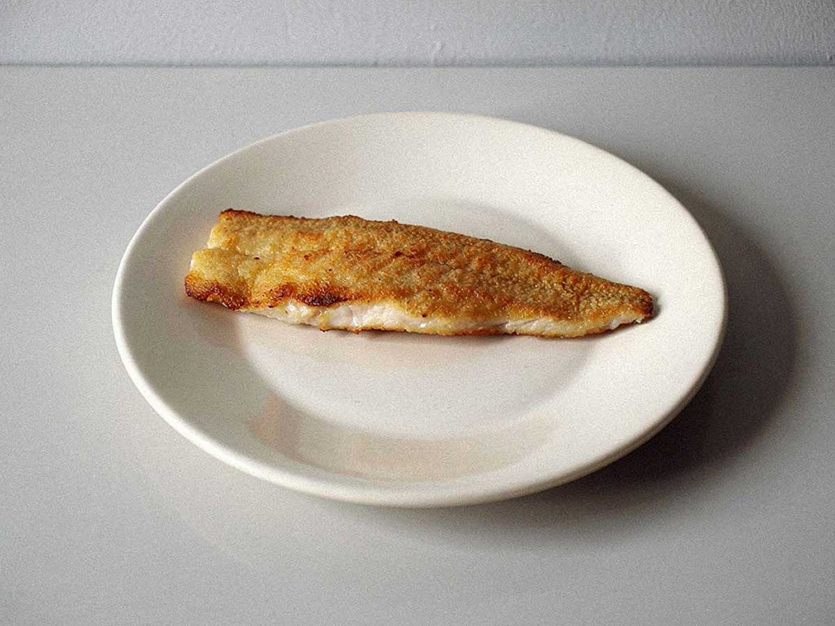 Een gebakken wijtingfilet op een wit bordje.