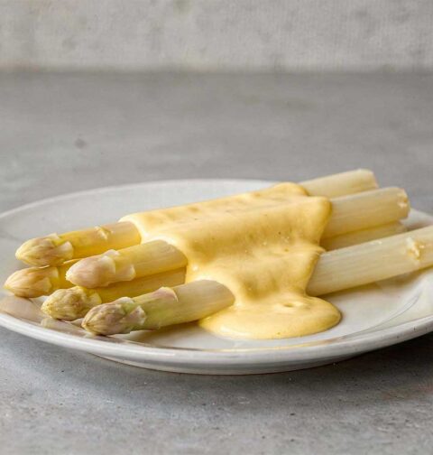 Witte asperges op een bordje, met daarover een Hollandaisesaus.