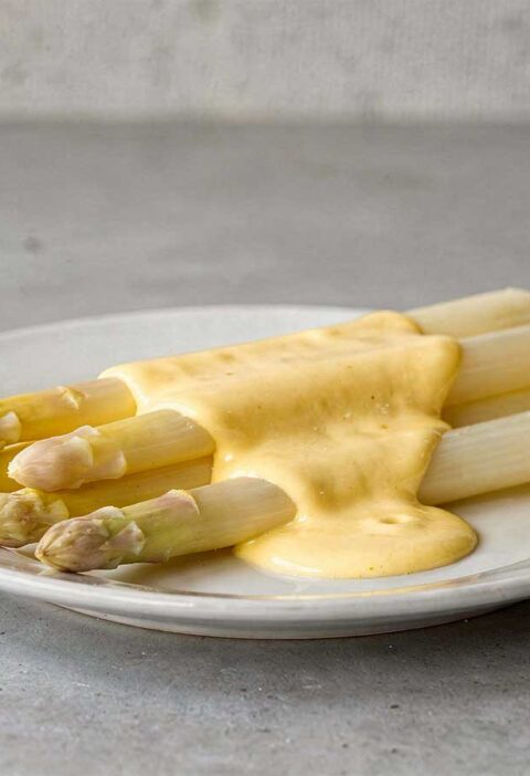 Witte asperges op een bordje, met daarover een Hollandaisesaus.