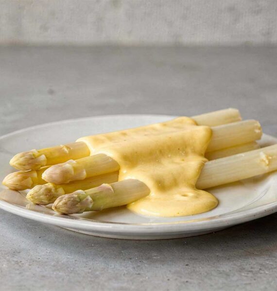 Witte asperges op een bordje, met daarover een Hollandaisesaus.