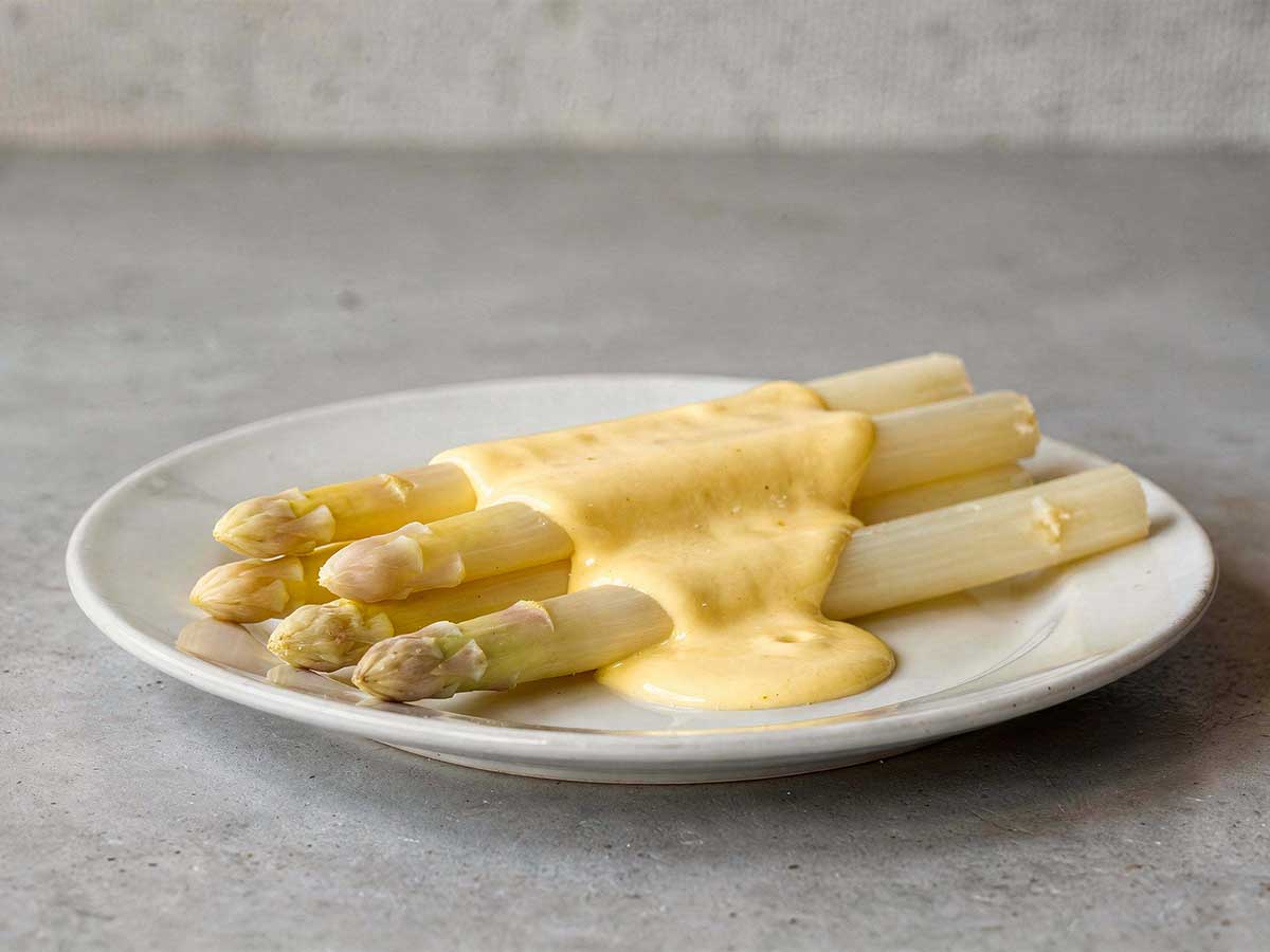 Witte asperges op een bordje, met daarover een Hollandaisesaus.