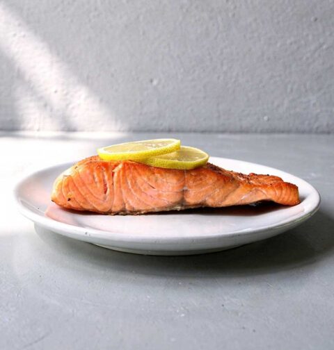 Een gebakken zalmfilet met schijfjes citroen op een wit bordje.
