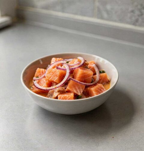 Een wit schaaltje met zalm ceviche en rode uien.