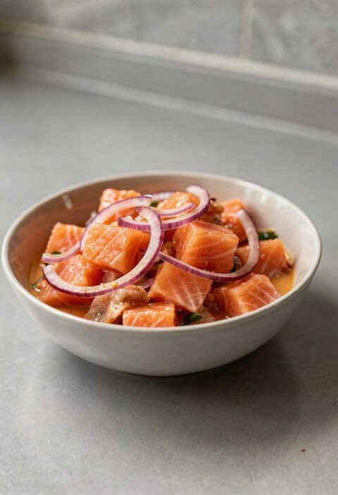 Een wit schaaltje met zalm ceviche en rode uien.