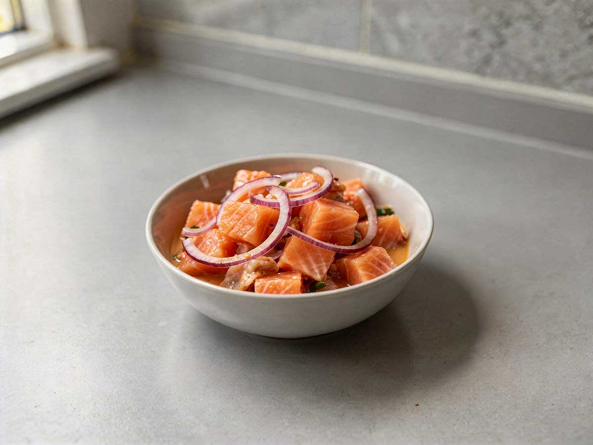 Een wit schaaltje met zalm ceviche en rode uien.