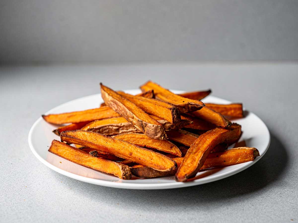 Een bordje met zoete aardappel friet, gebakken in een oven.