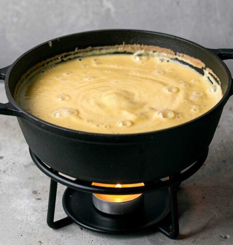 Een zwarte fonduepan op een theelichtje, met daarin Zwtserse kaasfondue.