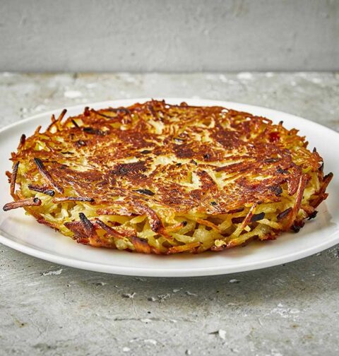 Een hele Zwitserse rösti op een wit bord.