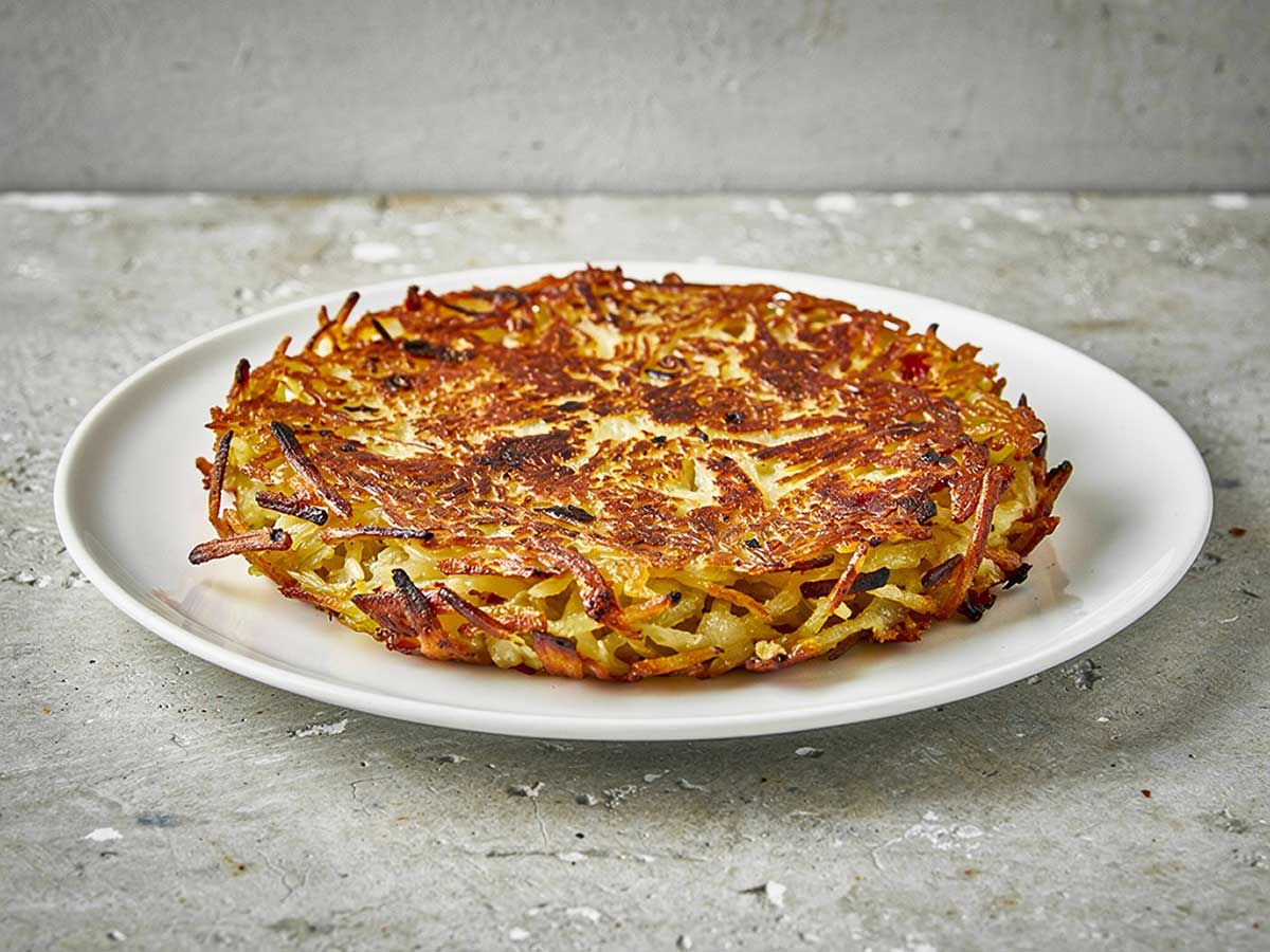 Een hele Zwitserse rösti op een wit bord.