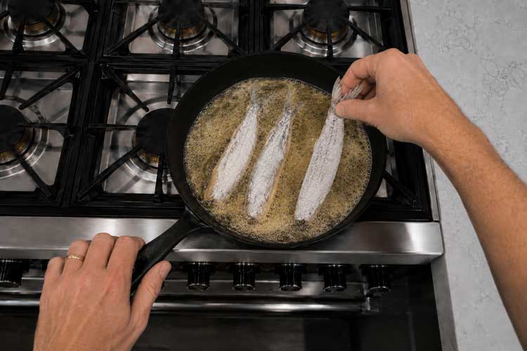 Als de olie heet is, leg je de haringen voorzichtig in de pan