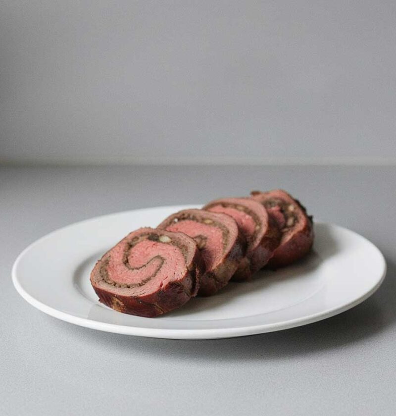 4 plakken van een gevulde bavette rollade op een witte schaal.