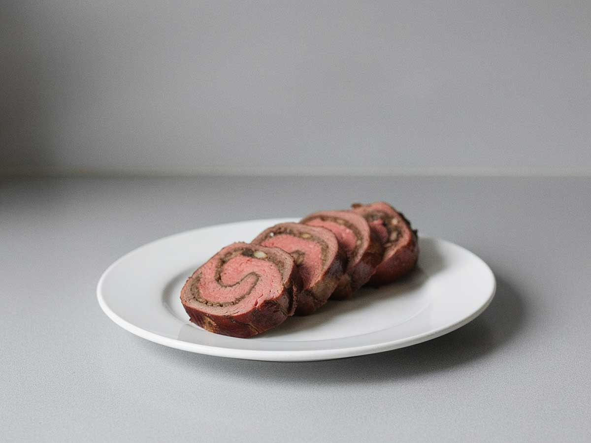 4 plakken van een gevulde bavette rollade op een witte schaal.