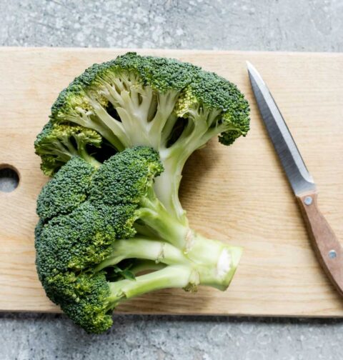 2 delen broccoli stronk liggen op een hout snijplank om gesneden en gekookt te worden.