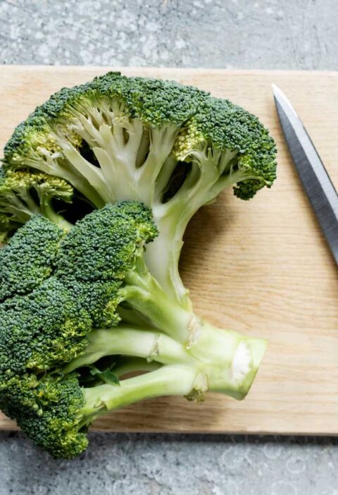 2 delen broccoli stronk liggen op een hout snijplank om gesneden en gekookt te worden.