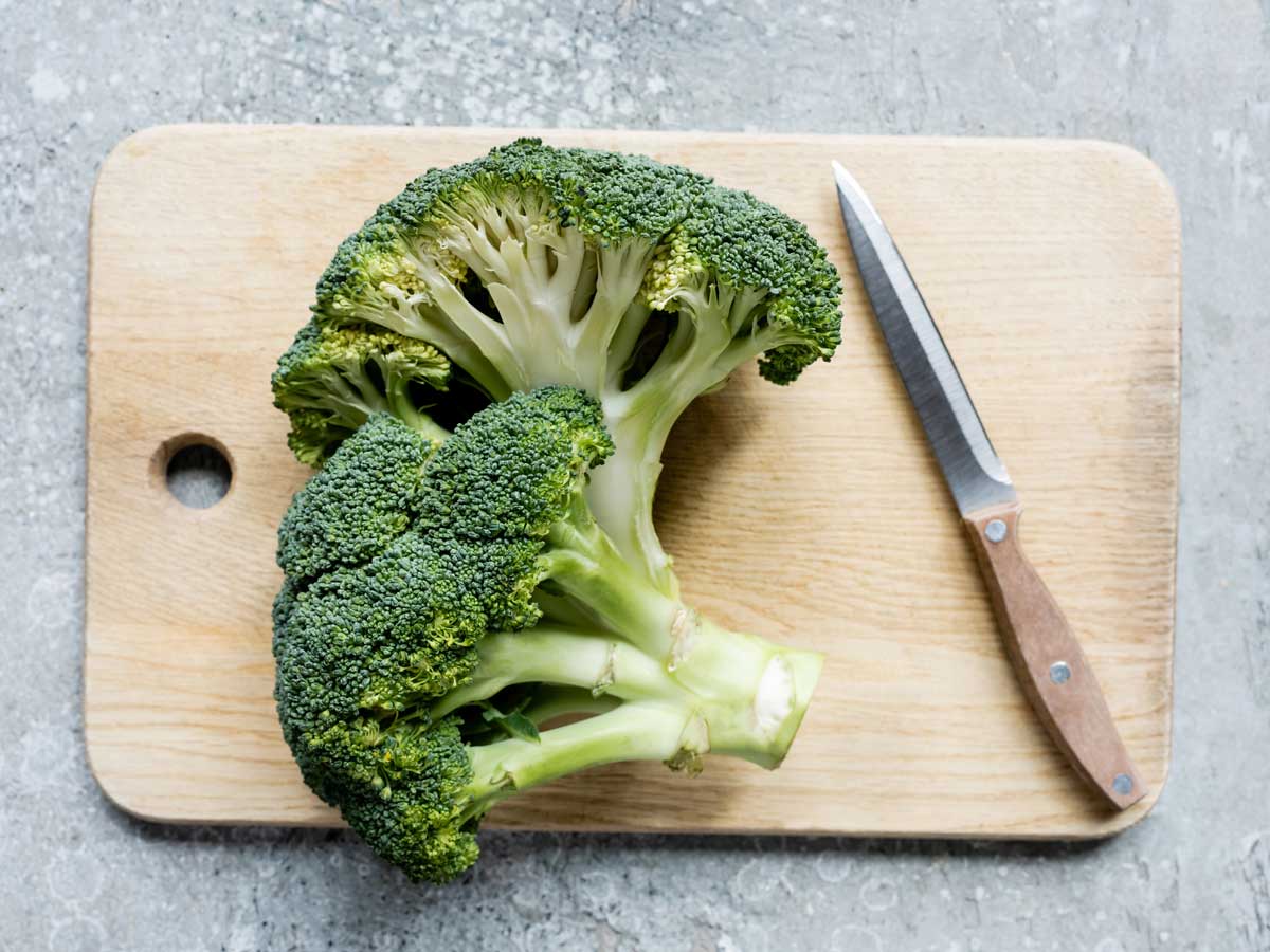 2 delen broccoli stronk liggen op een hout snijplank om gesneden en gekookt te worden.