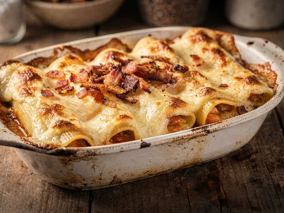 Zelfgemaakte cannelloni met bechamelsaus en spekjes in een witte ovenschaal