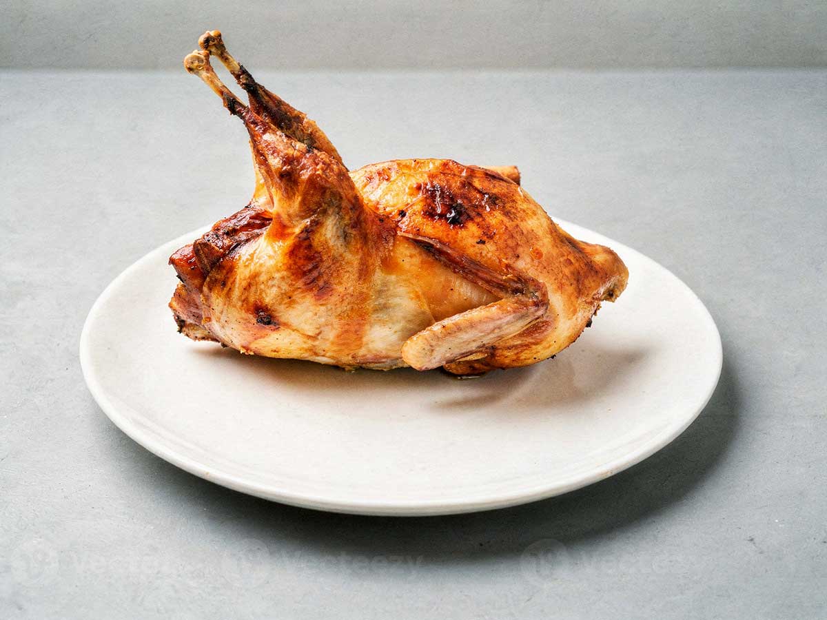 Een gebakken hele kwartel op een wit bordje.
