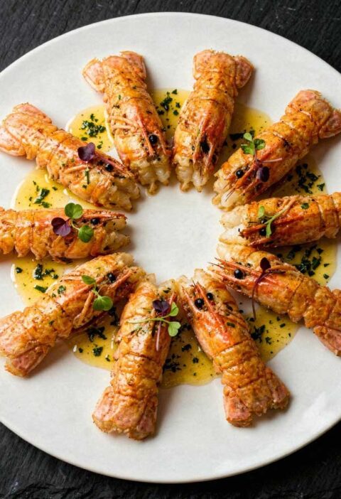 Gebakken langoustines sierlijk gerangschikt in een kring op een rond wit bord.