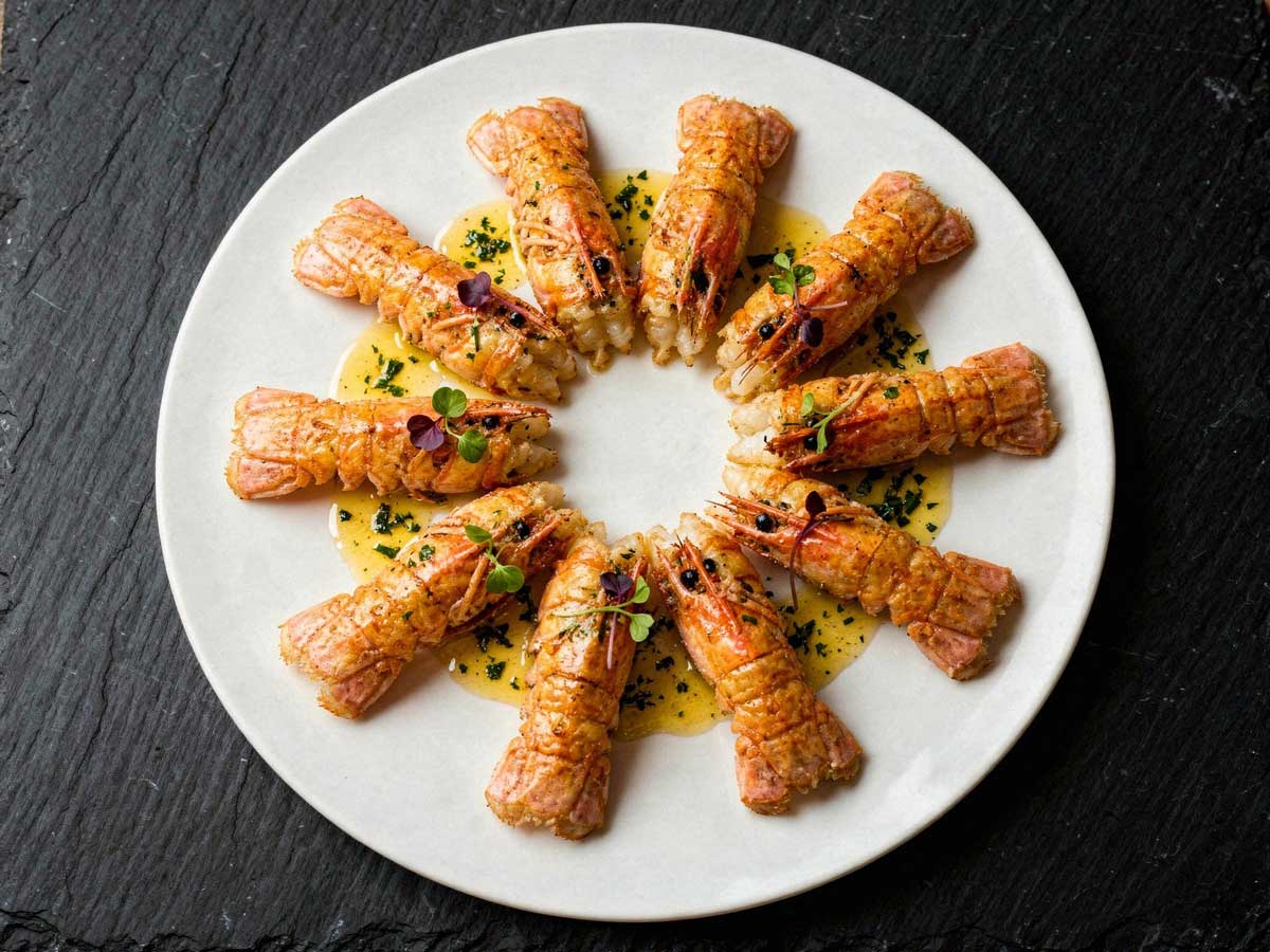 Gebakken langoustines sierlijk gerangschikt in een kring op een rond wit bord.