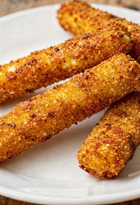 Vier hele gefrituurde mozzarellasticks losjes verspreid op een wit bord