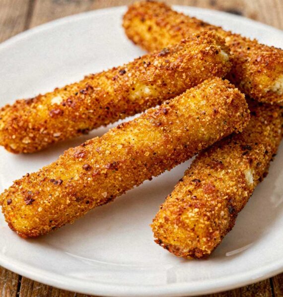 Vier hele gefrituurde mozzarellasticks losjes verspreid op een wit bord