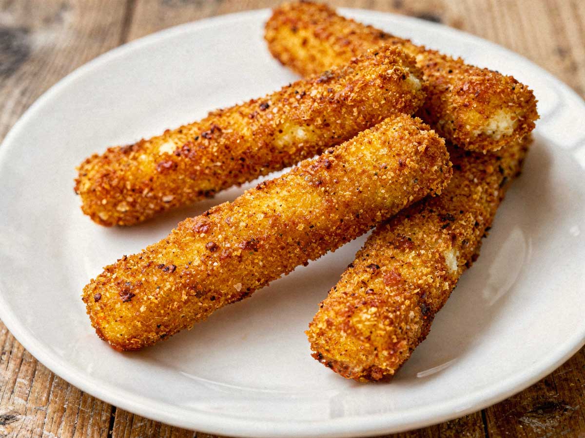 Vier hele gefrituurde mozzarellasticks losjes verspreid op een wit bord