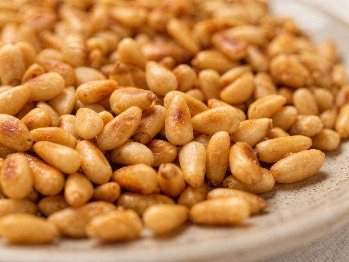 Goudbruin geroosterde pijnboompitten verspreid op een plat bord om af te koelen.