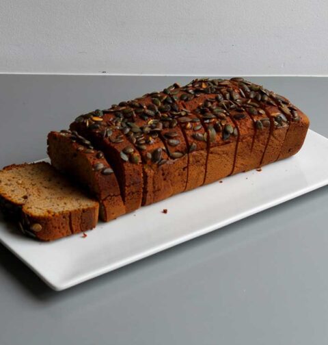 Een heel, in plakken gesneden, pompoenbrood op een witte schaal.