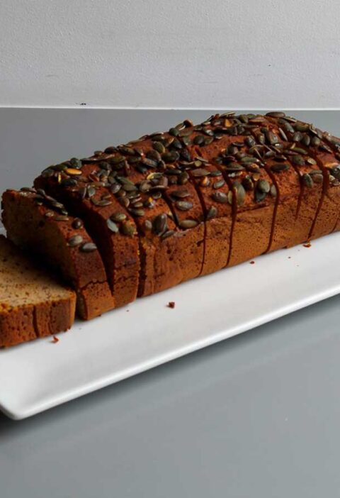 Een heel, in plakken gesneden, pompoenbrood op een witte schaal.