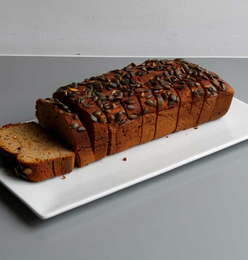 Een heel, in plakken gesneden, pompoenbrood op een witte schaal.