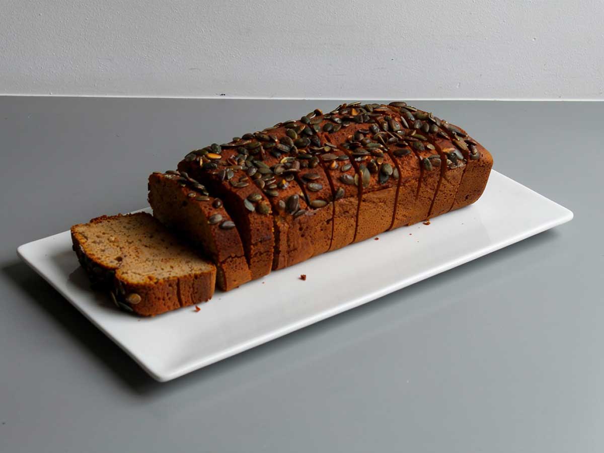 Een heel, in plakken gesneden, pompoenbrood op een witte schaal.