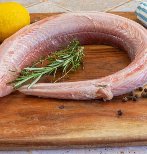 Een rauwe hondhaai ligt op een houten snijplank, klaar om in filets gesneden te worden.