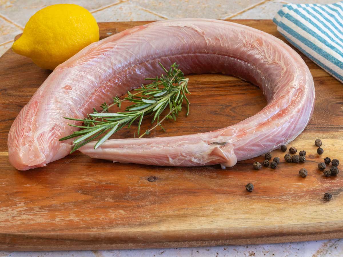 Een rauwe hondhaai ligt op een houten snijplank, klaar om in filets gesneden te worden.