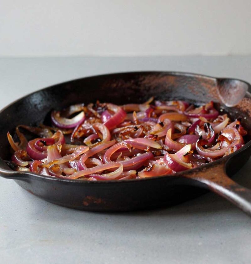 Een gietijzeren koekenpan met daarin gefruite of gebakken rode uien.
