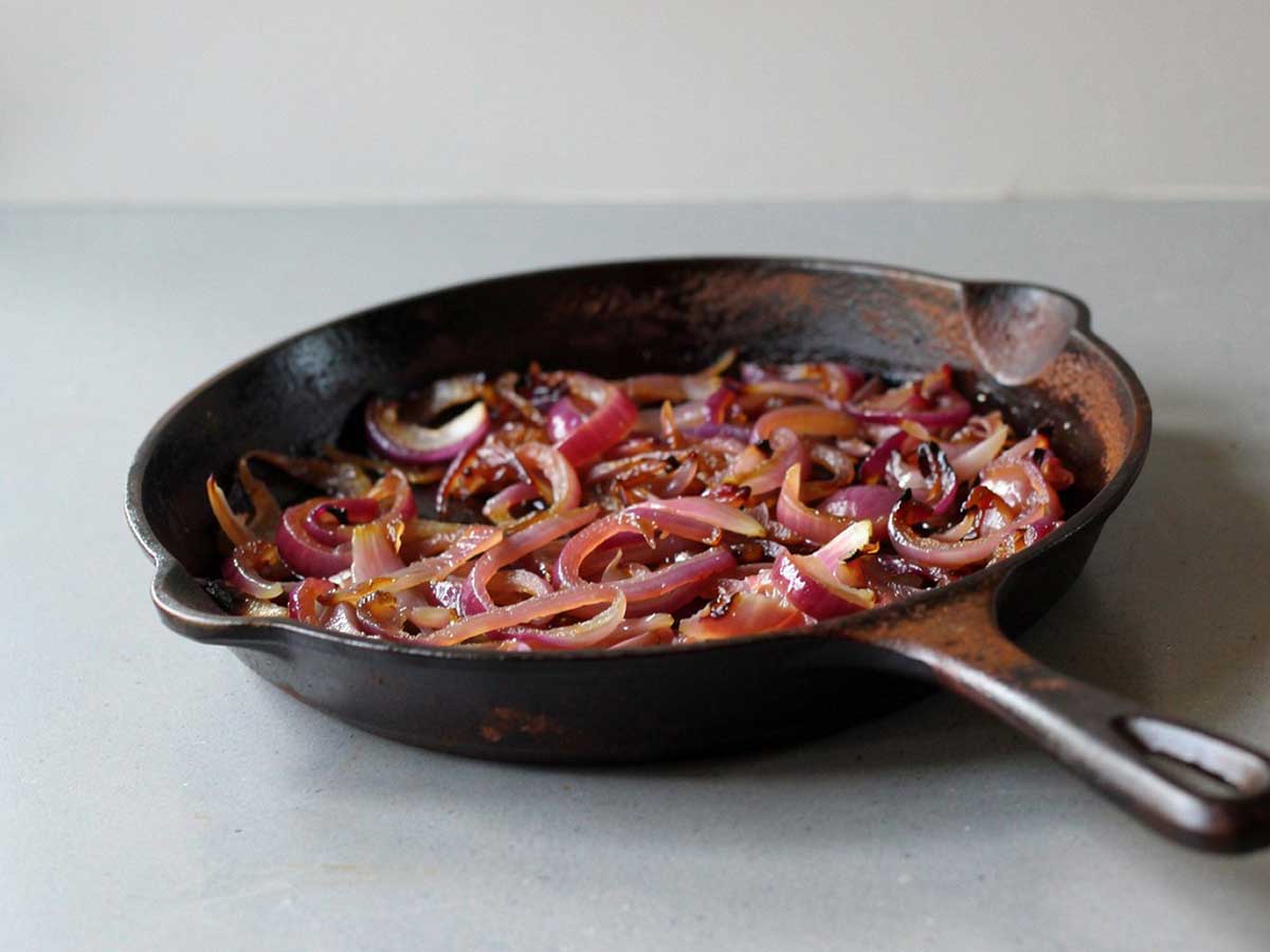 Een gietijzeren koekenpan met daarin gefruite of gebakken rode uien.