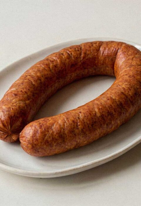 Een sappige, glanzende Hollandse rookworst op een plat wit bord zonder garnering.