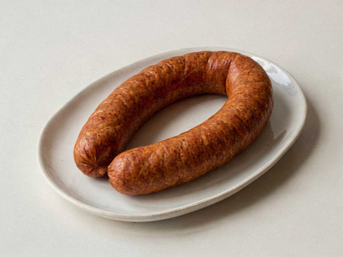 Een sappige, glanzende Hollandse rookworst op een plat wit bord zonder garnering.