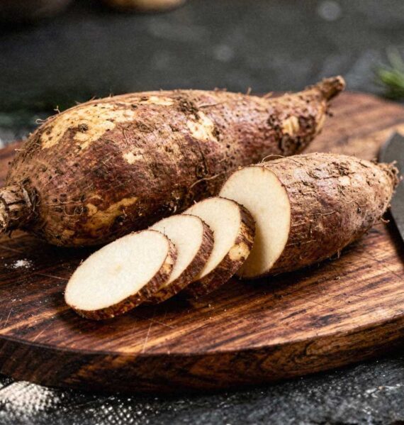 Twee rauwe yams op een snijplank waarvan één deels in plakken is gesneden.