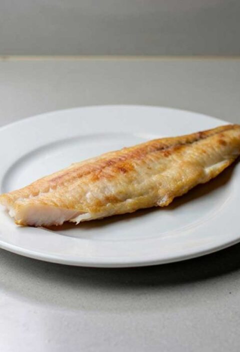 Een gebakken zeewolffilet op een wit bord.