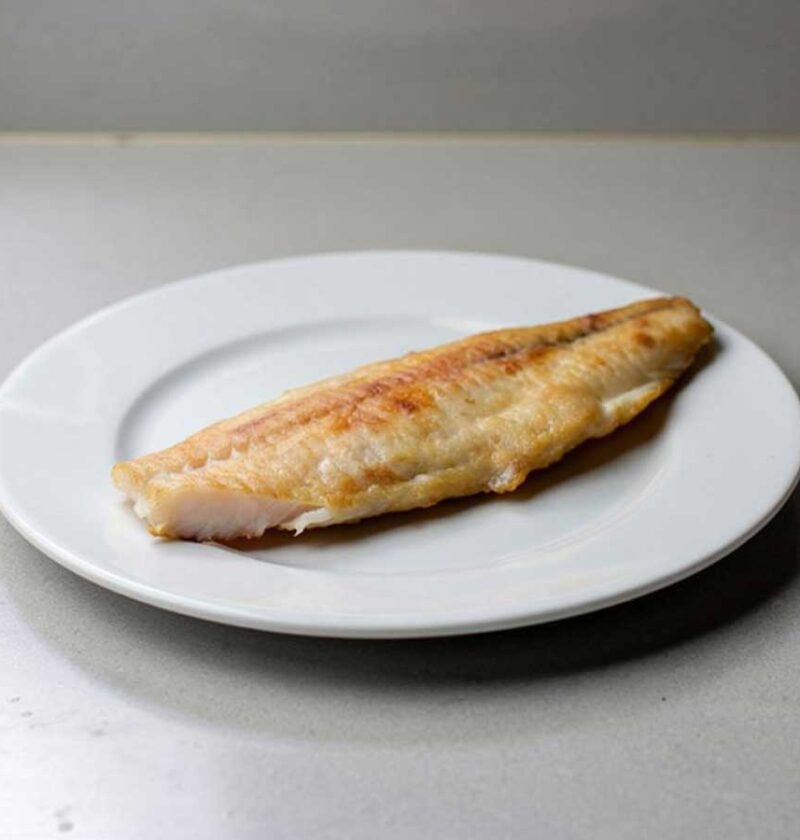 Een gebakken zeewolffilet op een wit bord.