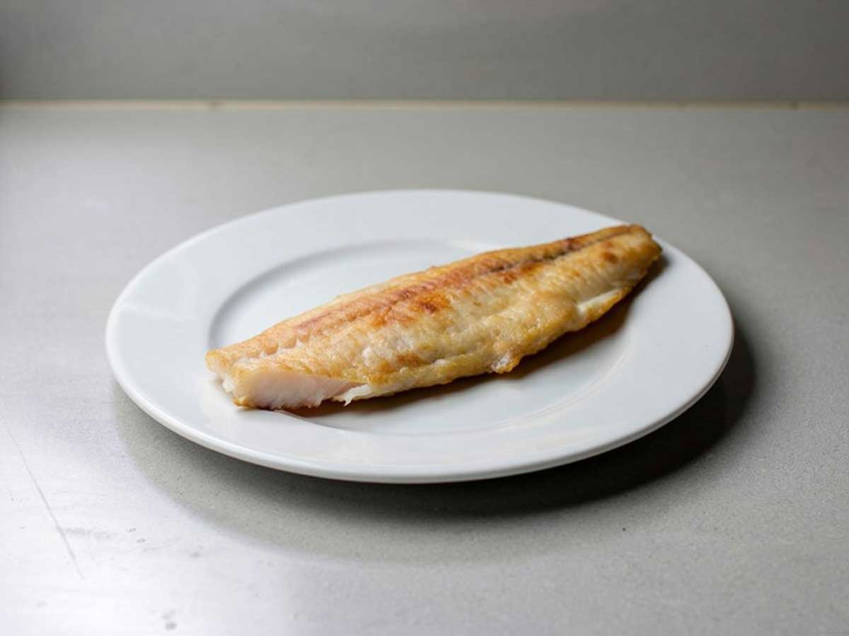 Een gebakken zeewolffilet op een wit bord.
