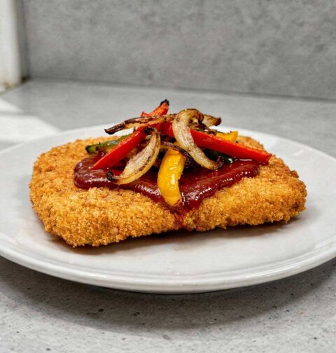 Een wit bord met daarop een gebakken en gegarneerde zigeunerschnitzel.