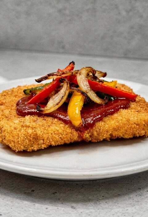 Een wit bord met daarop een gebakken en gegarneerde zigeunerschnitzel.
