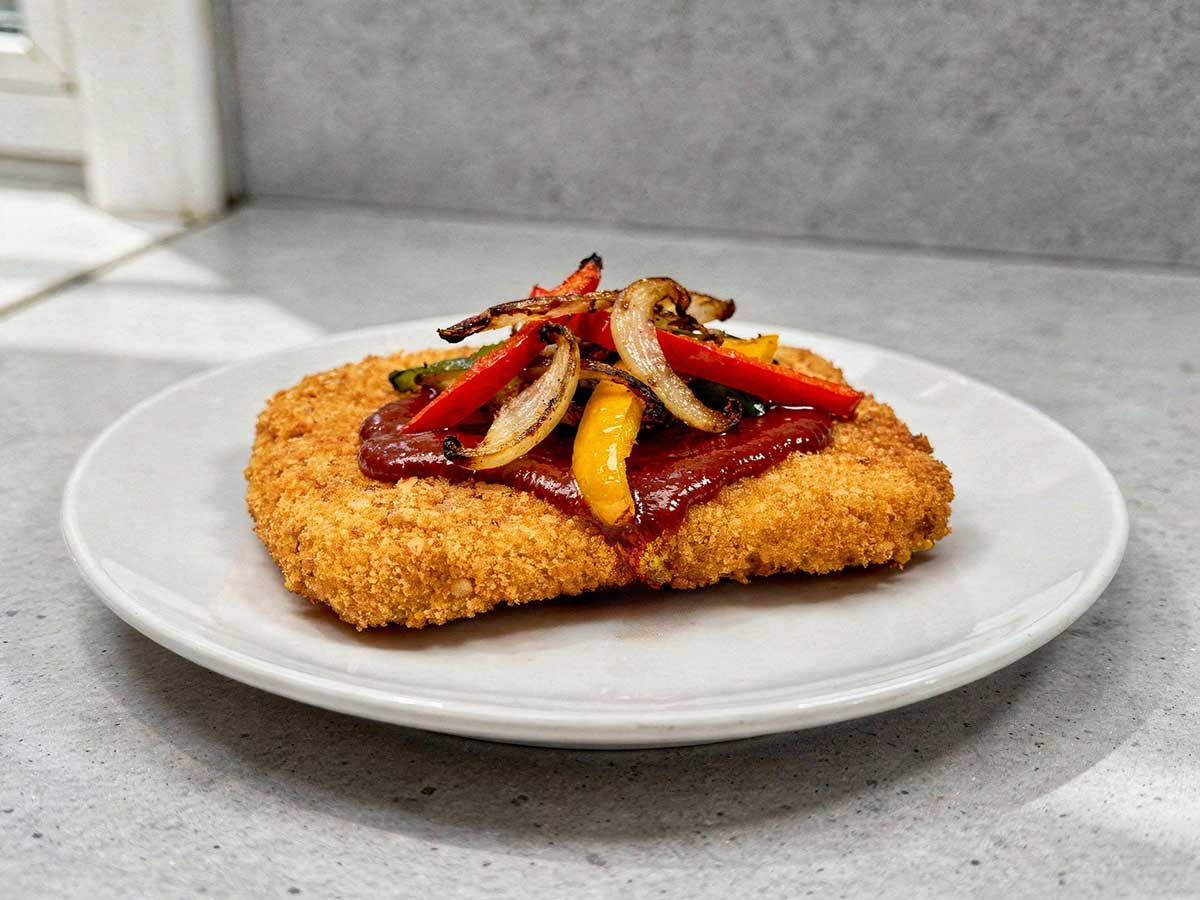 Een wit bord met daarop een gebakken en gegarneerde zigeunerschnitzel.