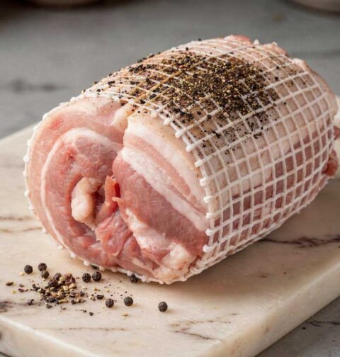 Rauwe spekrollade in een elastisch rolladenet op een marmeren snijplank met peperkorrels